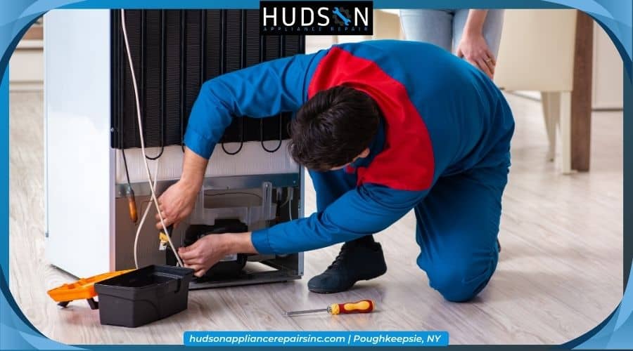 Appliance repair technician working on the back of a refrigerator with Hudson Appliance Repair branding.