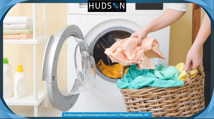balance-front-load-washer - A person taking clothes from a wicker laundry basket to load into a white front-loading washing machine, featuring the Hudson Appliance Repair logo.