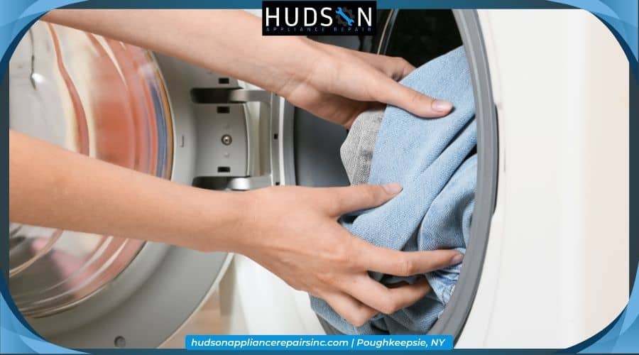 level-washing-machine-feet - Close-up of hands loading blue jeans into a front-loading washing machine, featuring a Hudson Appliance Repair logo.